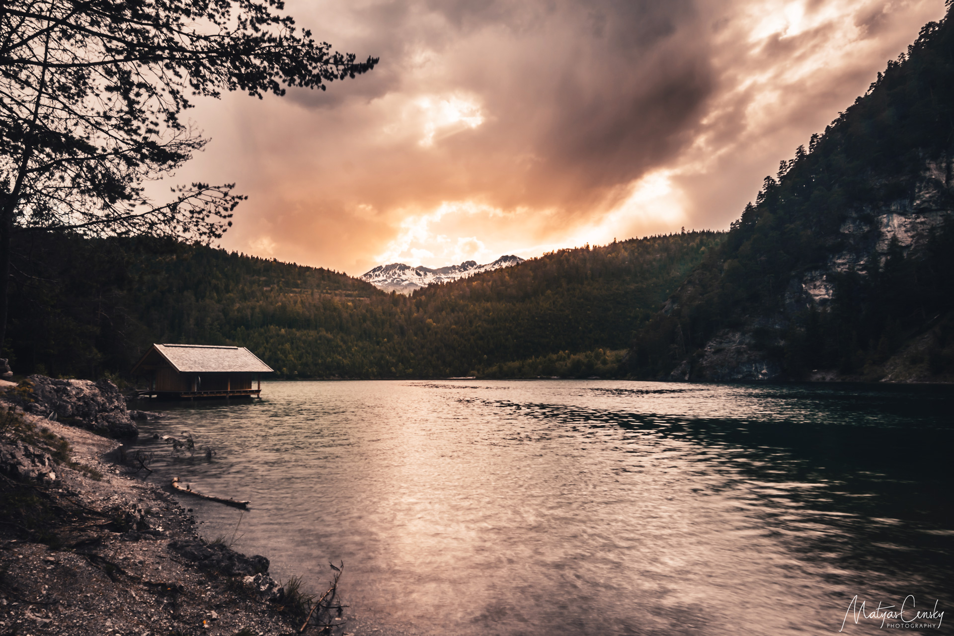 Photo of a sunset over Blinsee, Austria, with wooden hut on a shore.