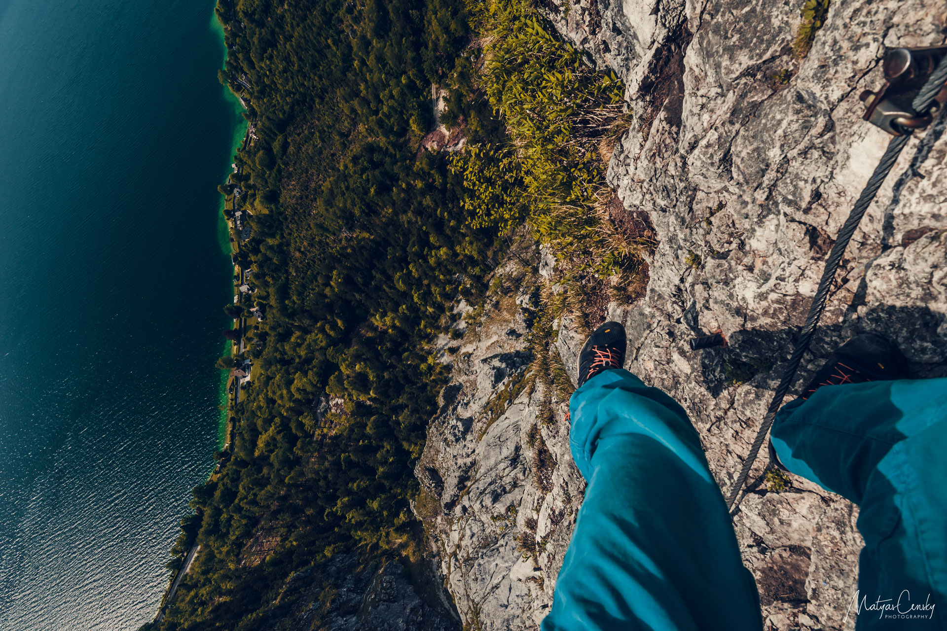 Photo of photographer/climber legs hanging from the rock wall looking down on Attersee.