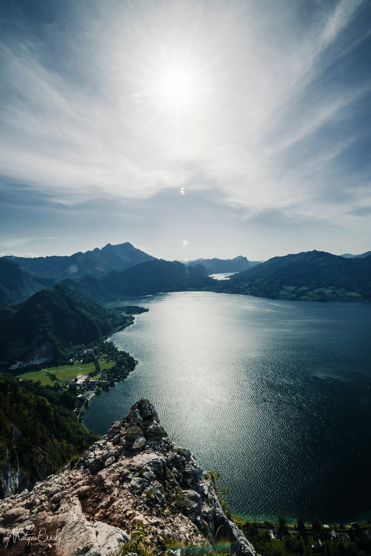Landscape photo of Attersee in mid day from via ferrrata with a rock in the foreground and Mondsee in the background.