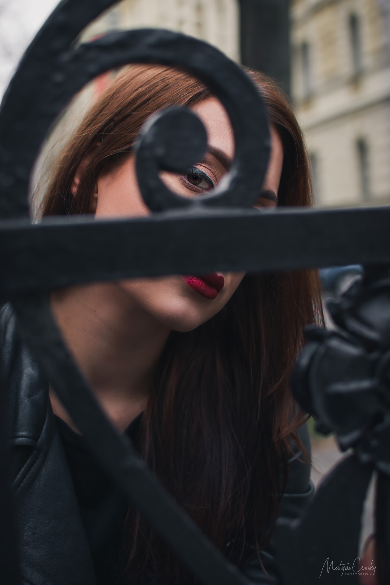 Close up photo of dark red hair women through old iron decorative fence copying the shape of golden ratio around her eye.
