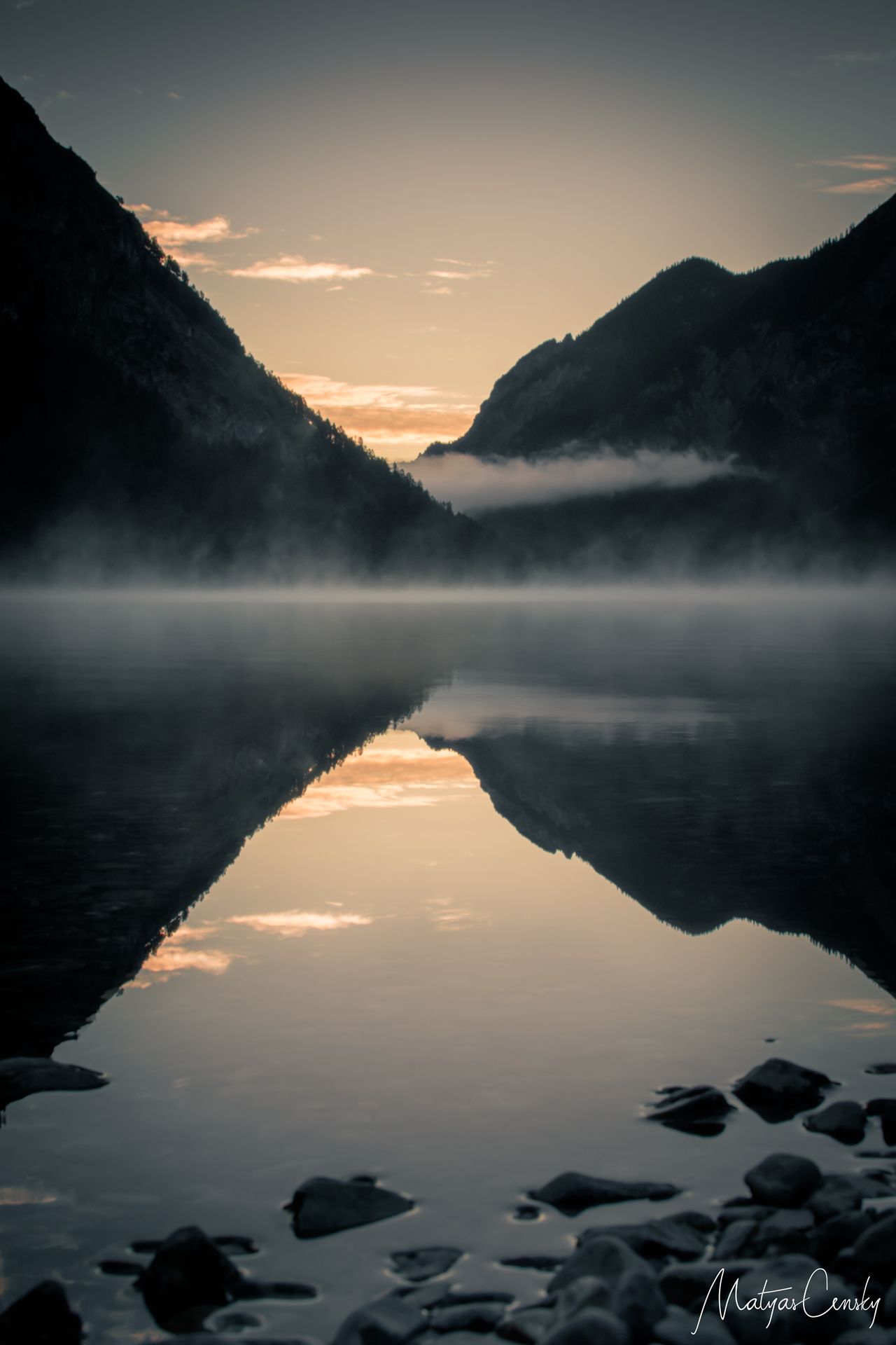 Sunrise over Heiterwanger See, Austria with morning myst over the lake and clear reflection of the sun rise with silluette of the mountains in the still water.