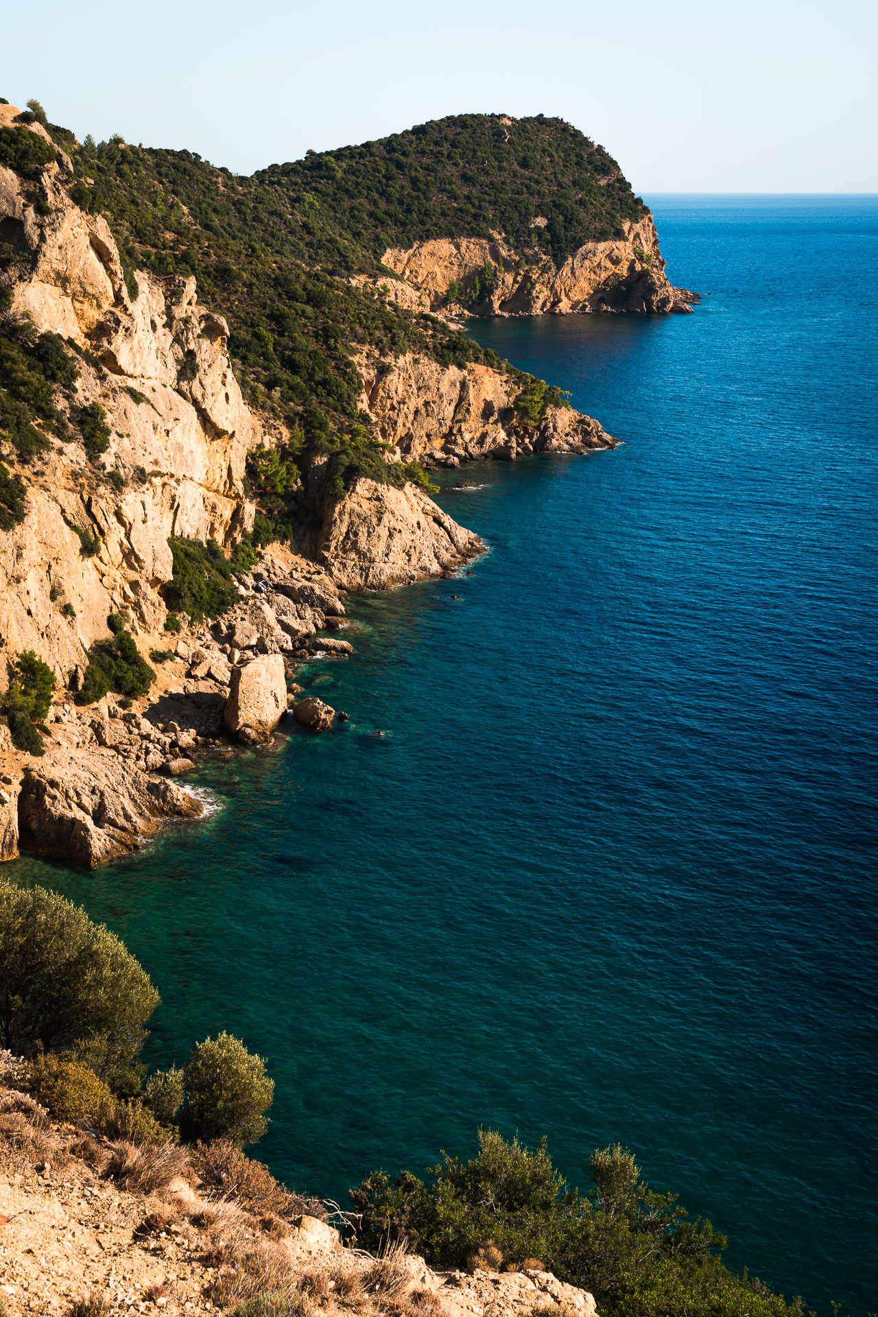 Photo of orange cliffs and blue sea with a car wreck on the bottom in Thassos, Greece.