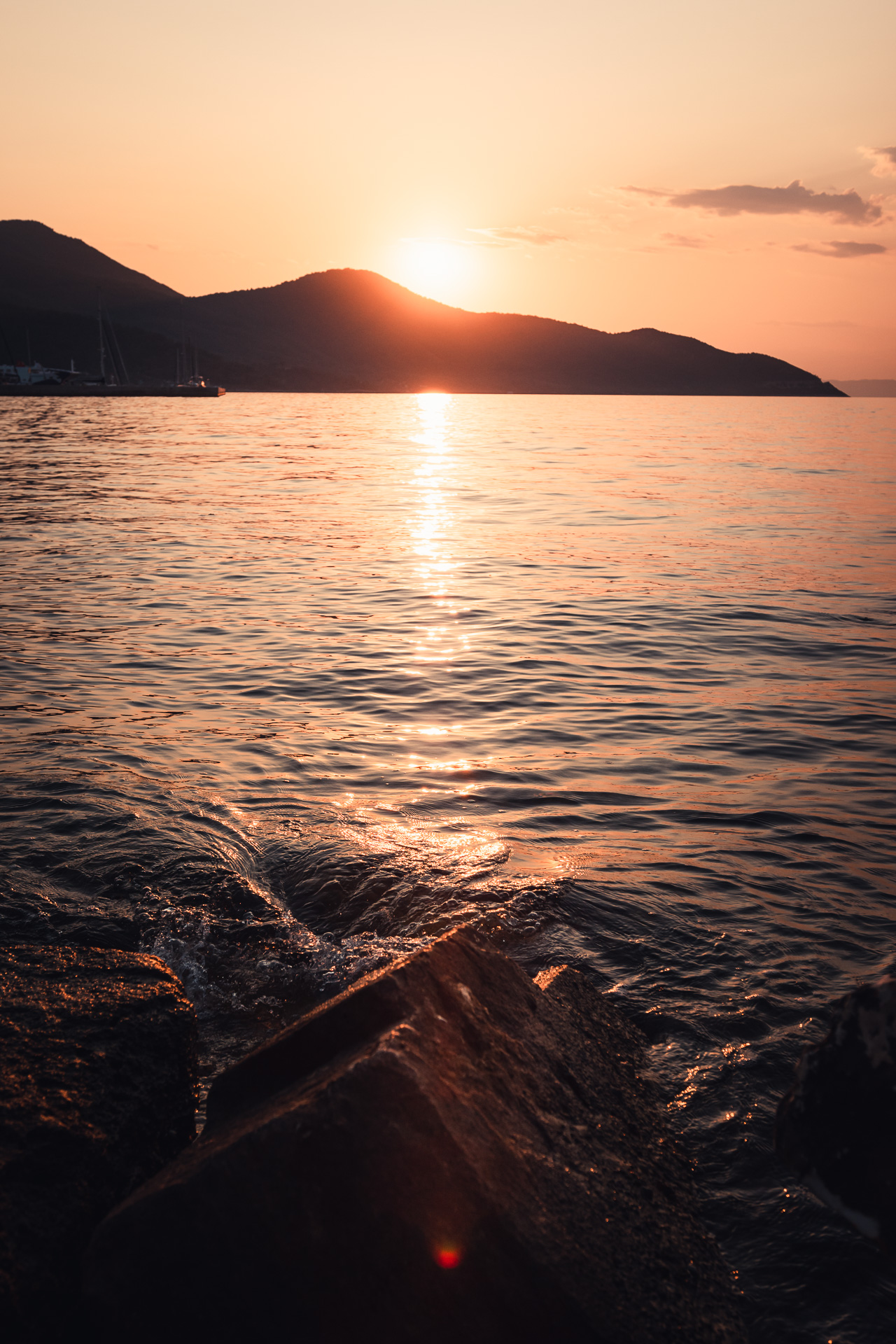 Photo of a sunset reflecting in a sea with a small wave breaking on a stone in Thassos, Greece.