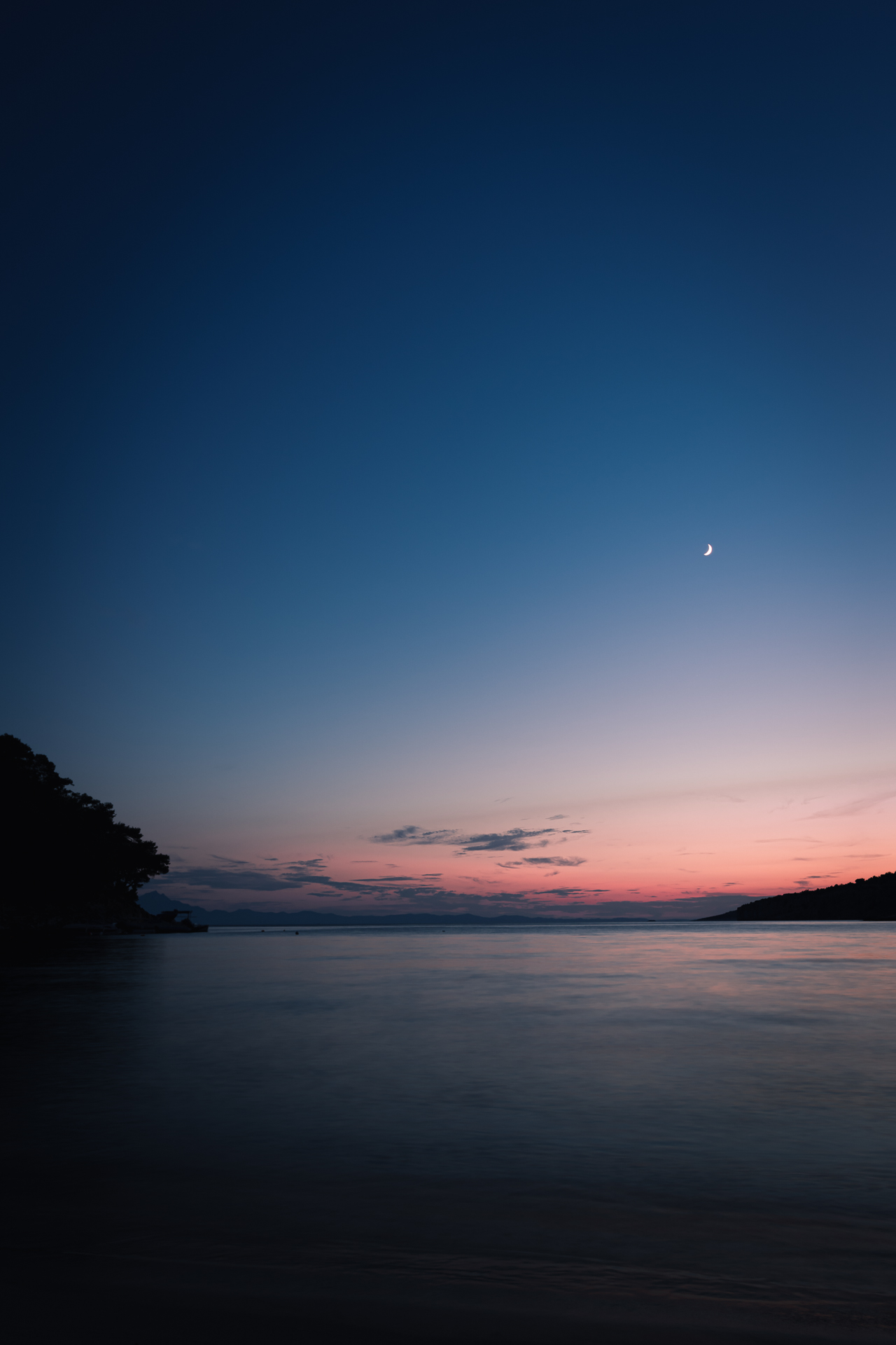 Photo of a moon in a distance over a beach at night in Greece.