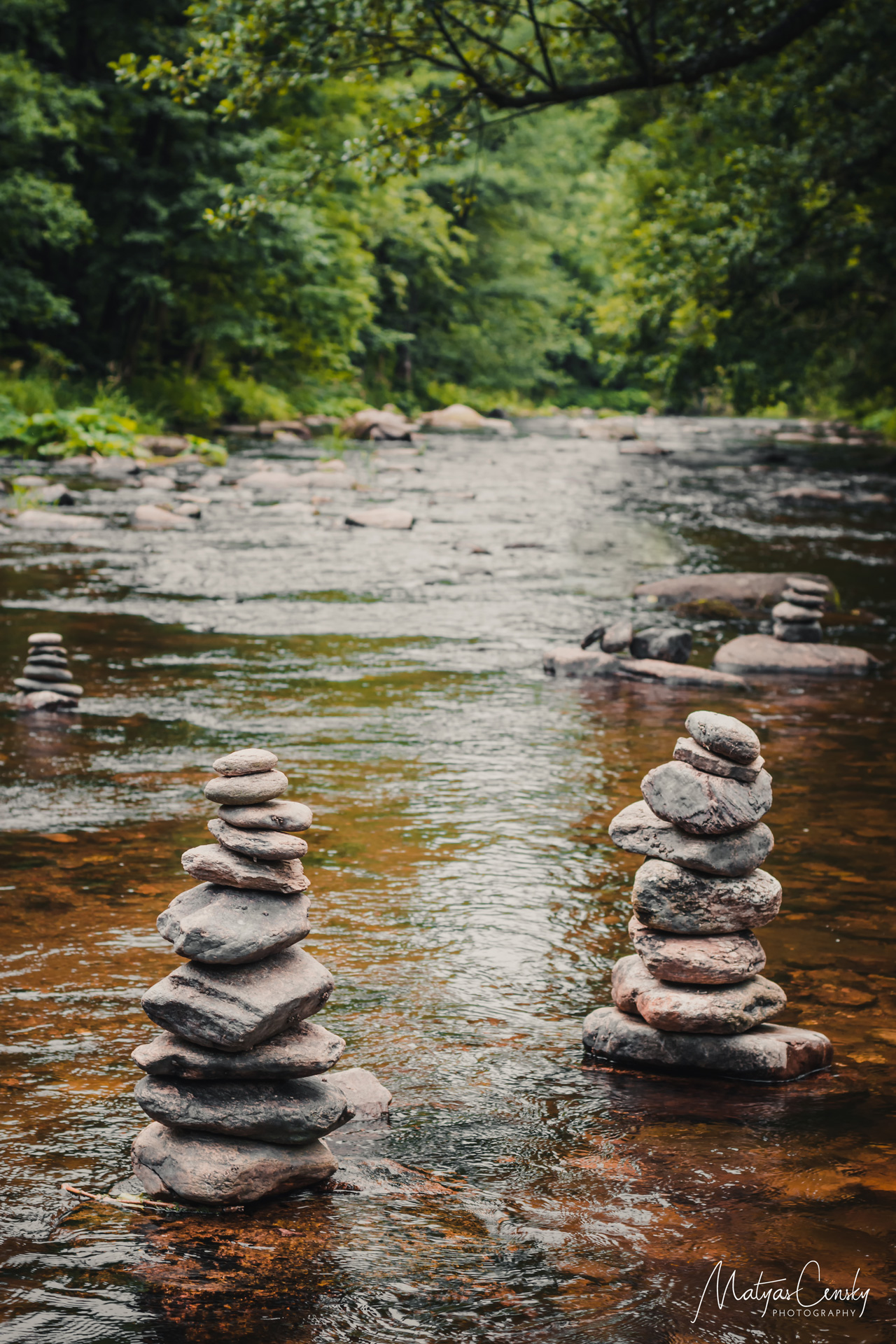 Photo of four statues of balanced stones in the river in a green forest.