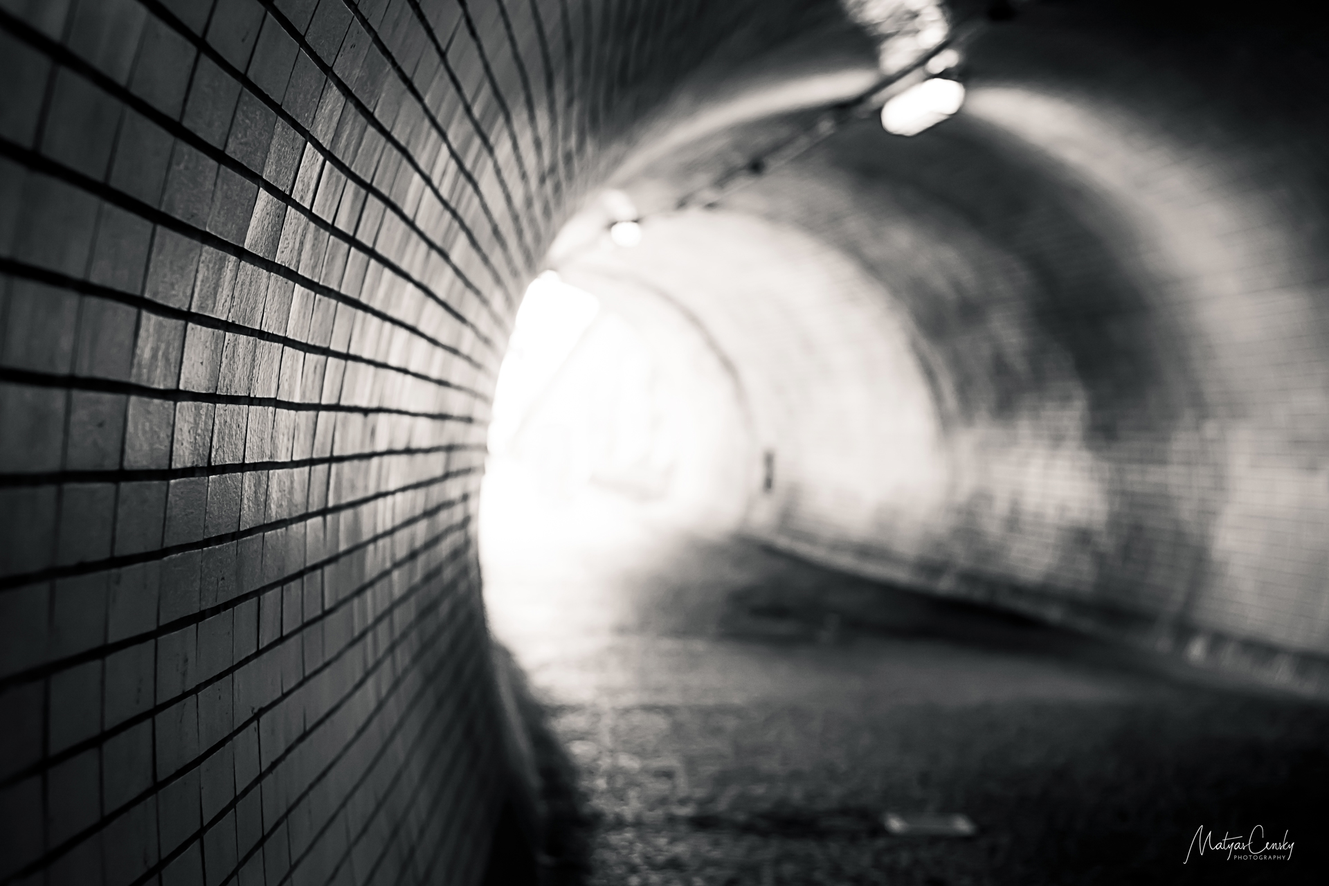 Black and white photo of a light at the end of a tunnel in Zizkov, Prague.