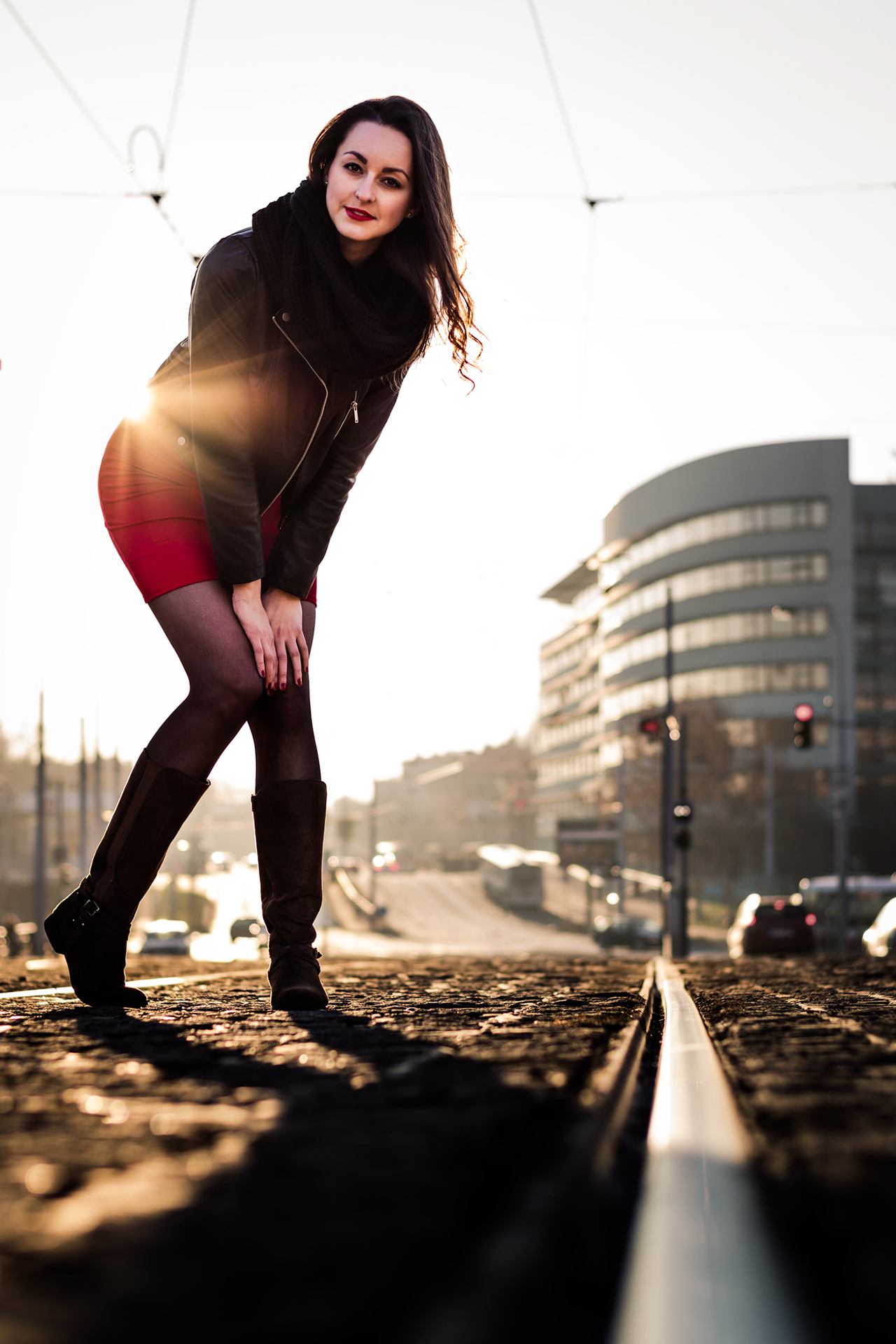 Full body photo of a female model posing on tram rails against the sunset.