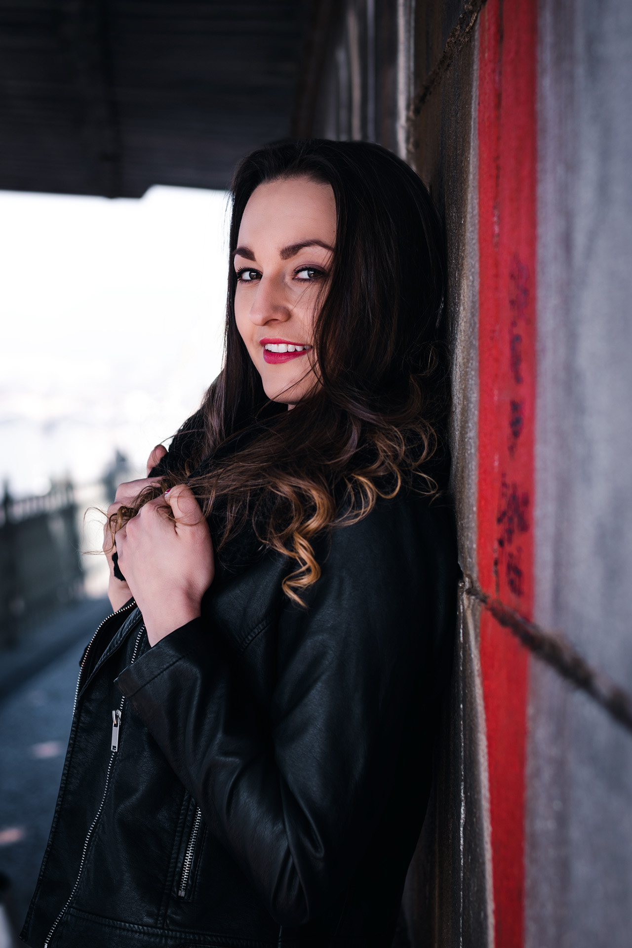 Photo of a female model in black leather jacket leaning against a graffity wall.