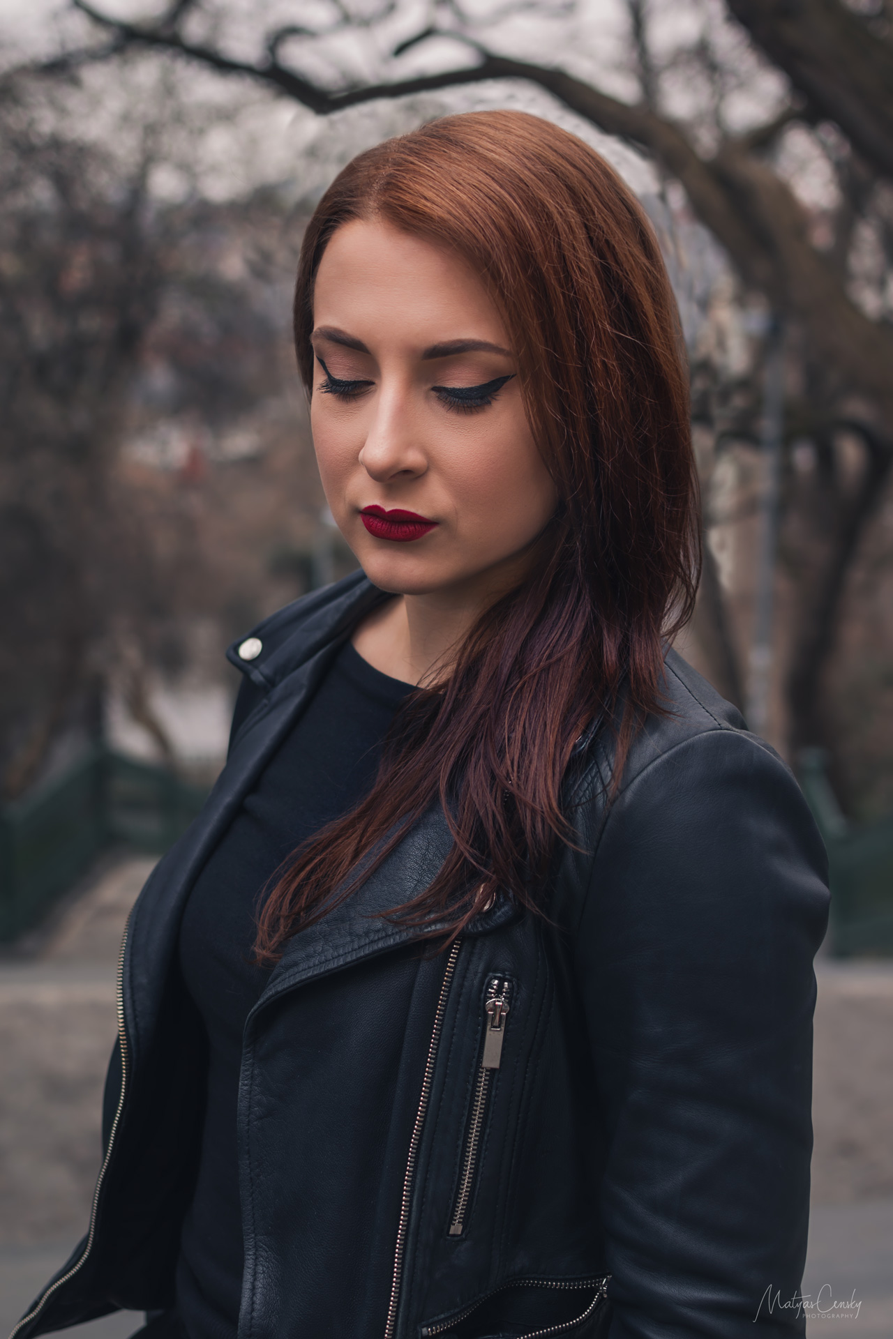 Half body shot of dark red hair women in black leather jacket and red lipstick looking down.