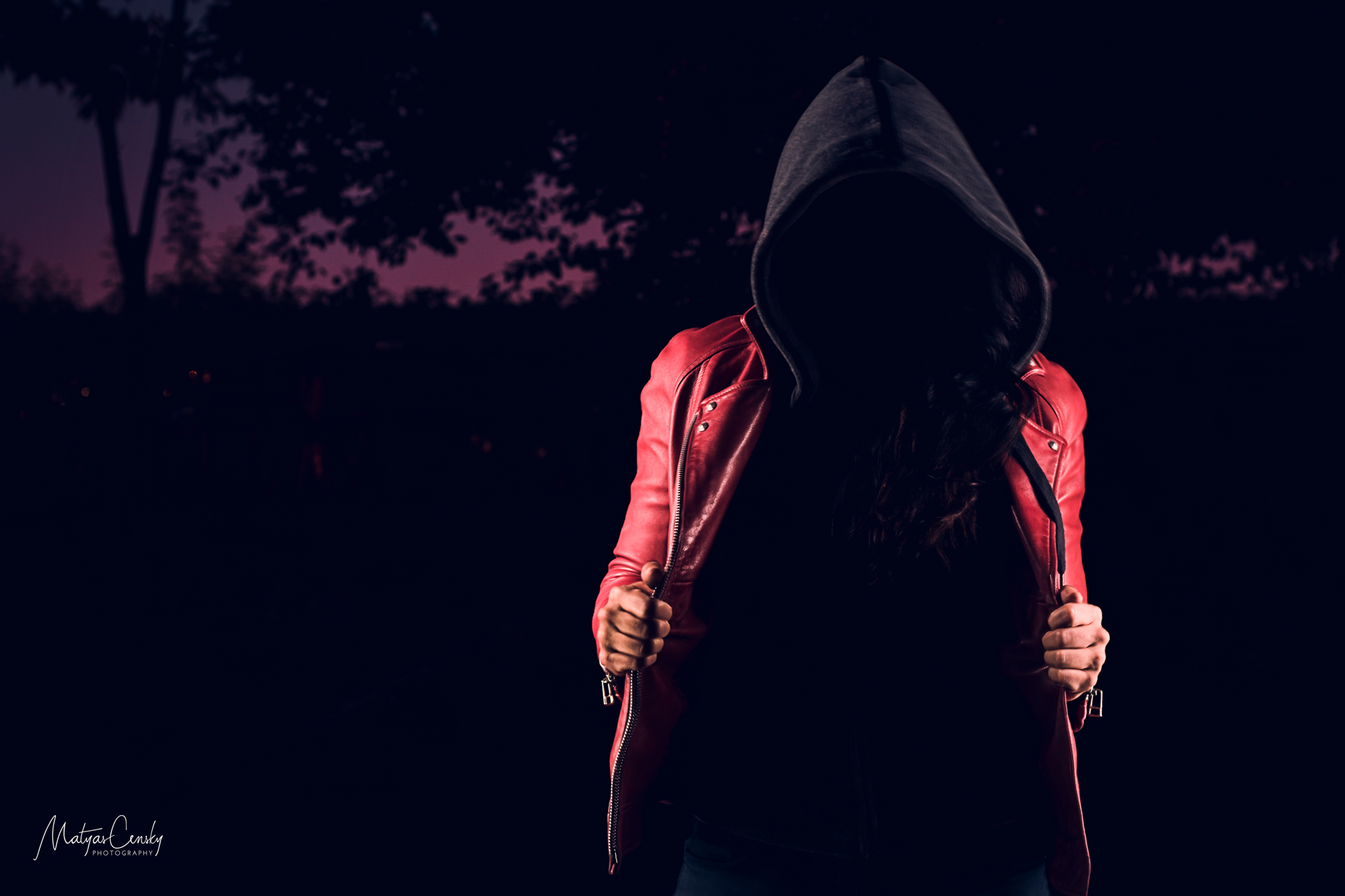 Night portrait of a model in red leather jacket and grey hood with no face.