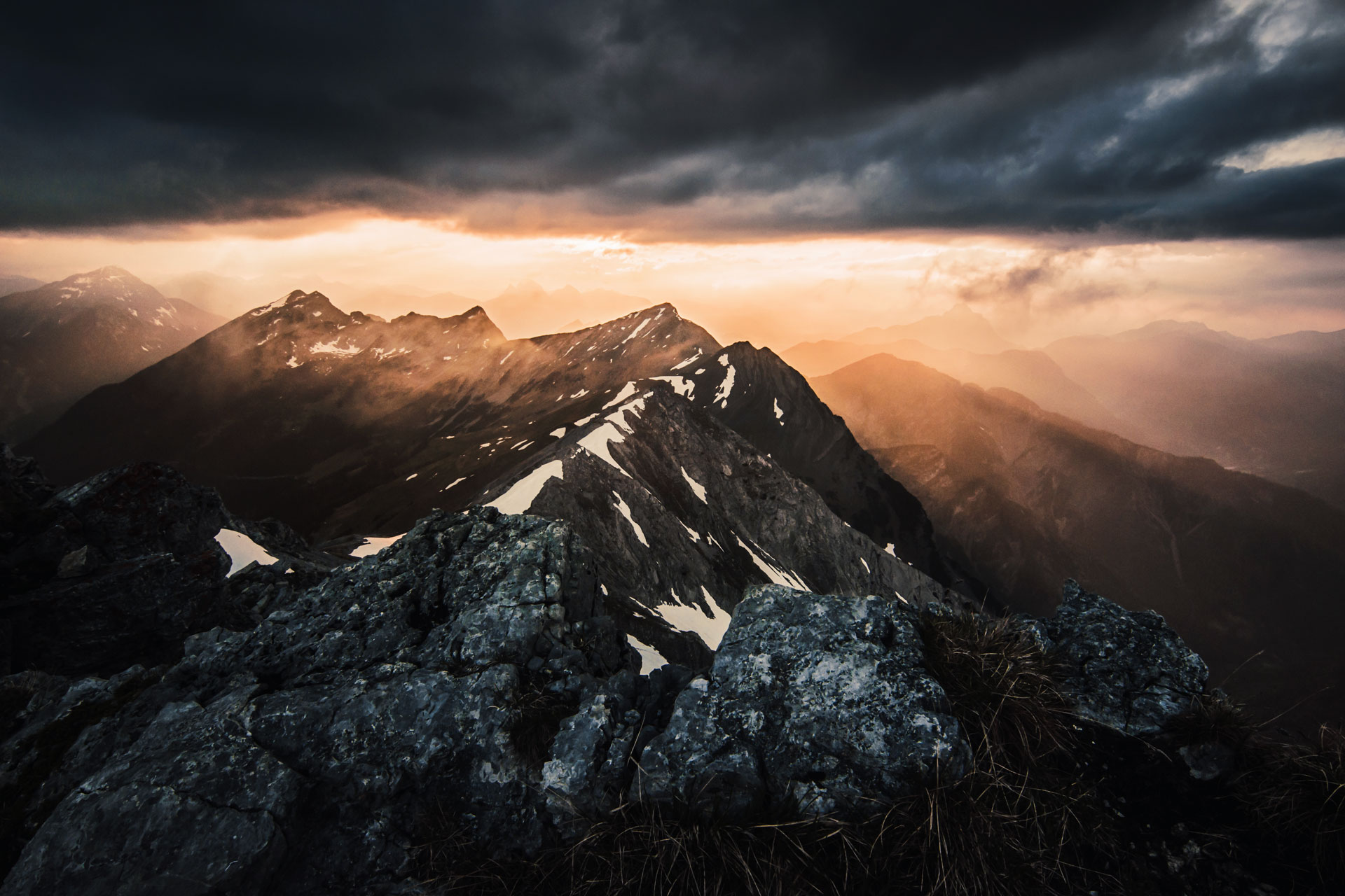 Photo of a sunset after a storm with mountain tops in the backgroung and rocks in the foreground taken from the top of Ups Spitze, Austria.